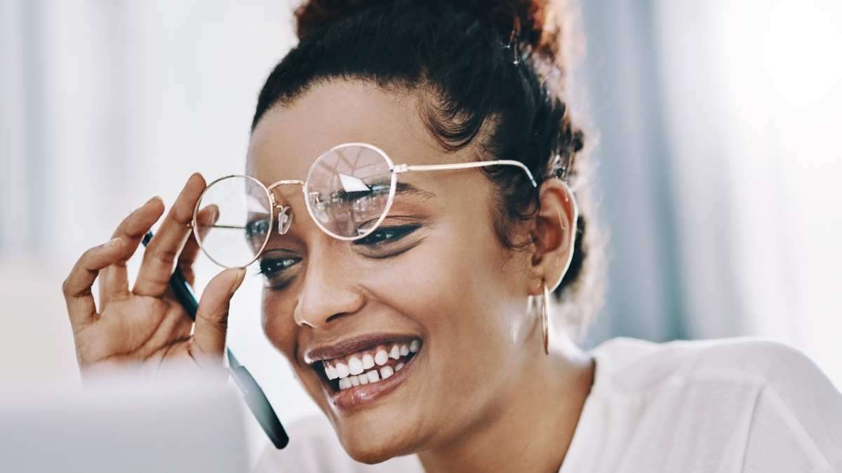 a woman smiling holding her glasses